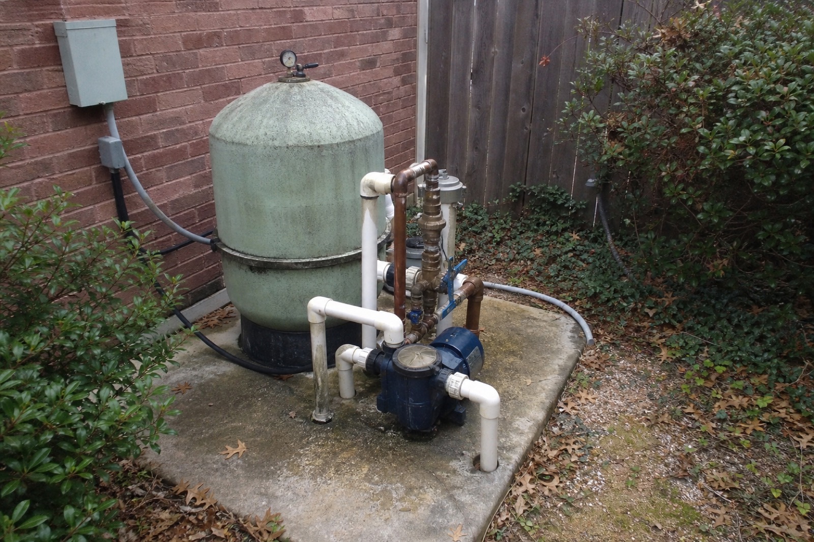 Pool equipment in a Plano backyard: aged filter tank, copper plumbing, navy pump.